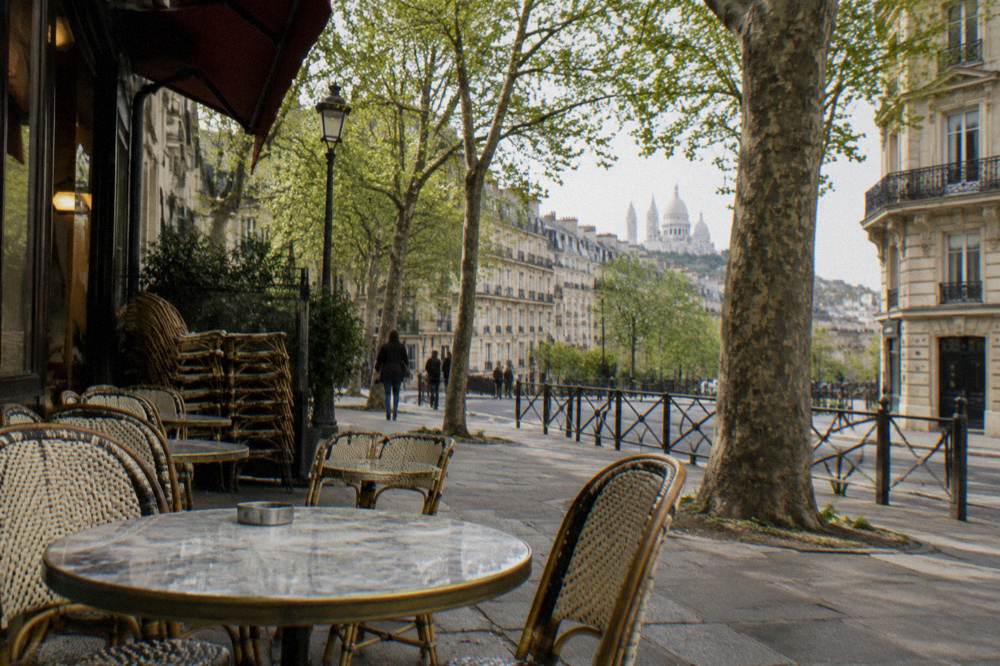 A Paris café terrace in early spring with chairs stacked and trees in new leaf