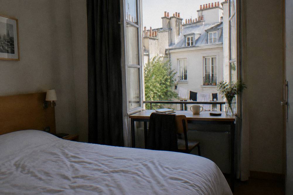 A simple hotel room with a double bed, desk and window onto a Paris courtyard