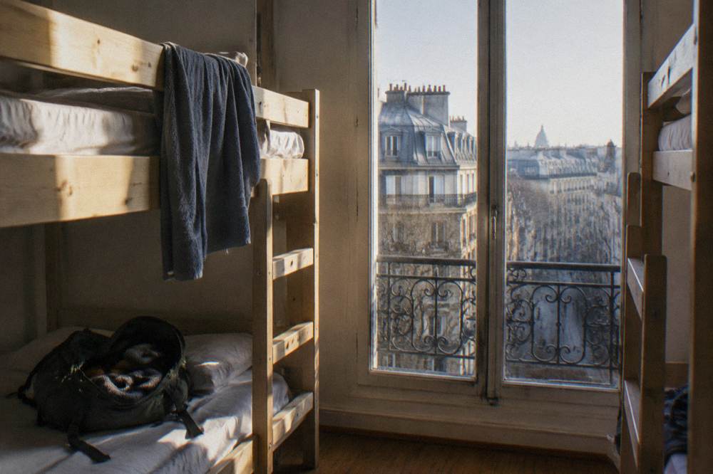A hostel dorm room with bunk beds and a large window letting in daylight