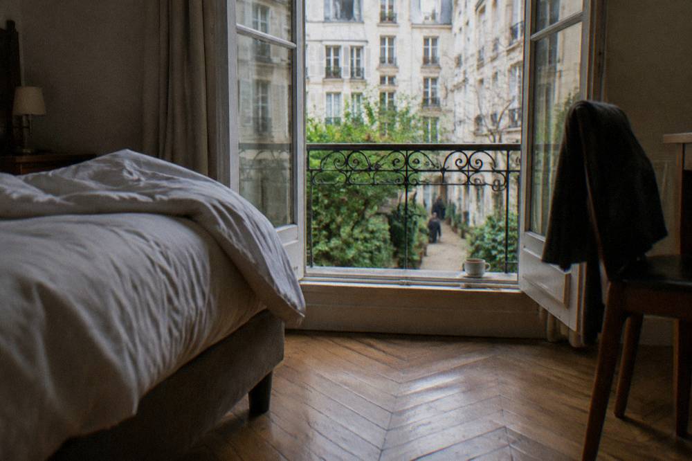 A small hotel room with a double bed, wooden floors and a window onto a Paris courtyard